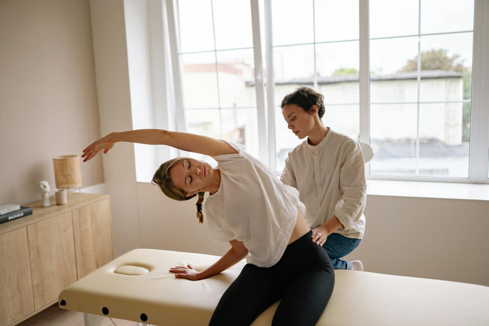 A woman receives a therapeutic massage and stretching on a massage table indoors.