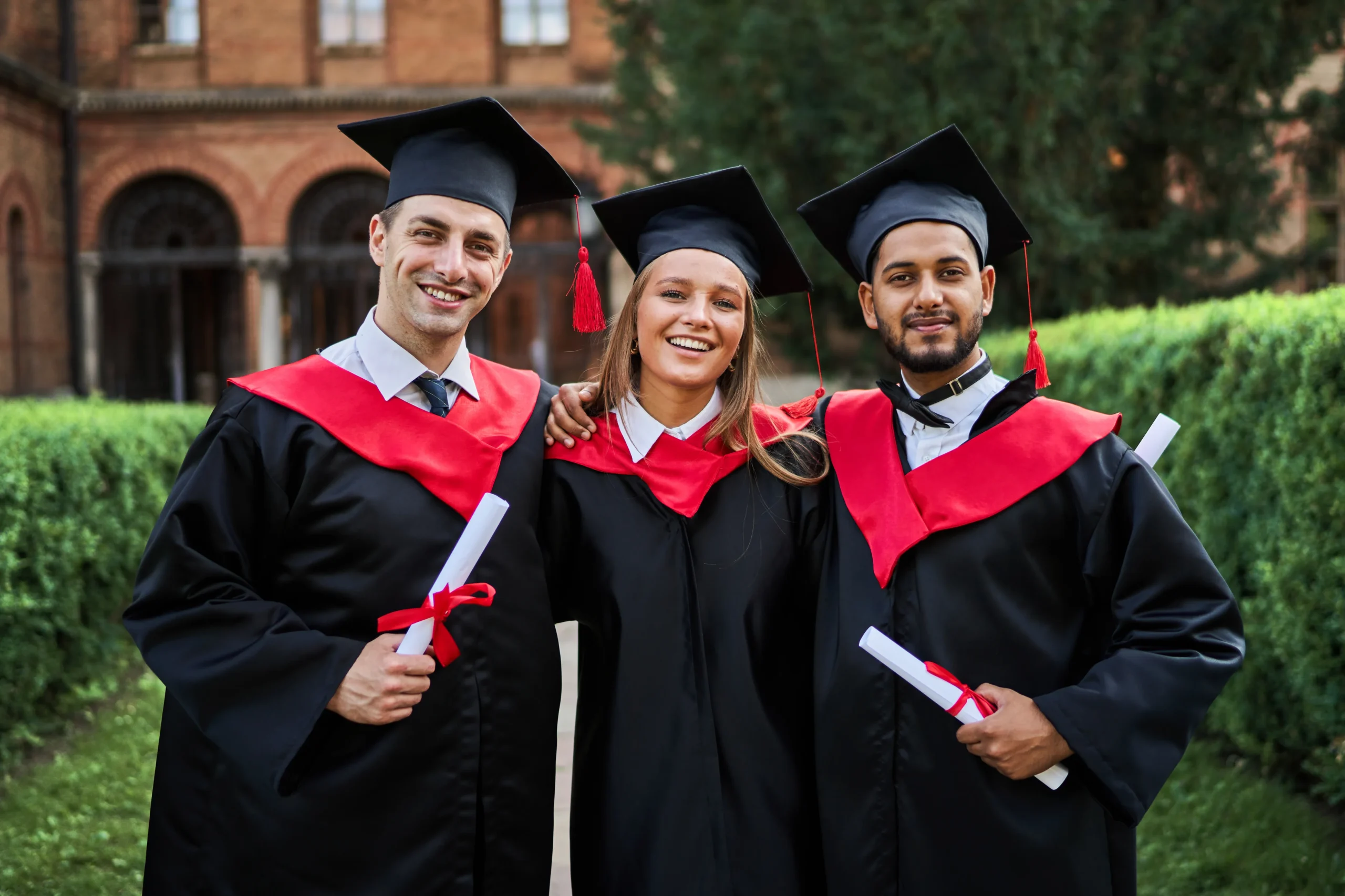 Graduates in red robes hug each other celebrating